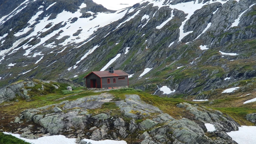 an old house on a rocky outcropping with snow on the mountains