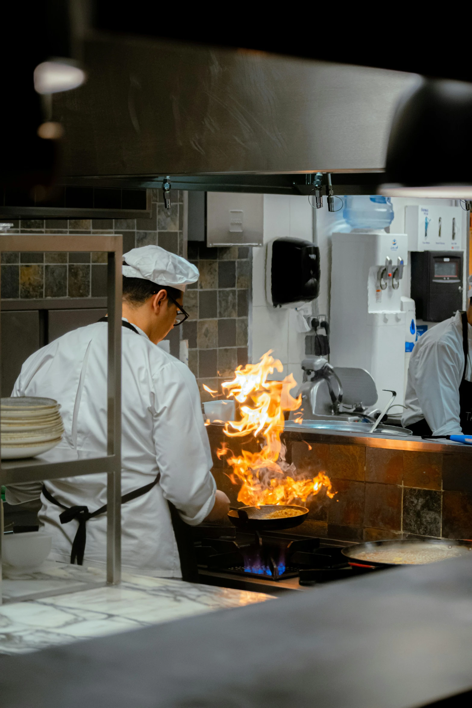 cooks cooking food inside a kitchen with flames coming out of it