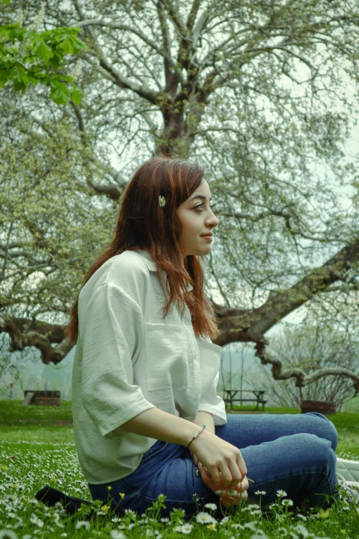 a woman sitting in the grass near a tree