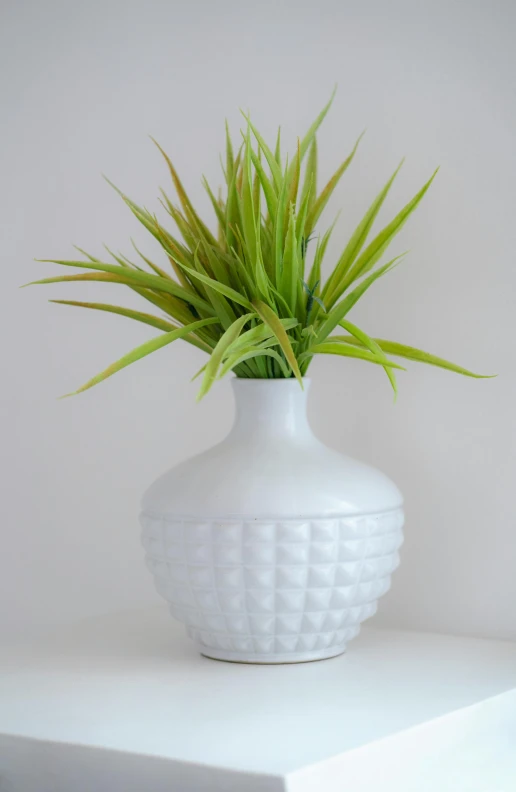 a white planter with grass in it sitting on a table