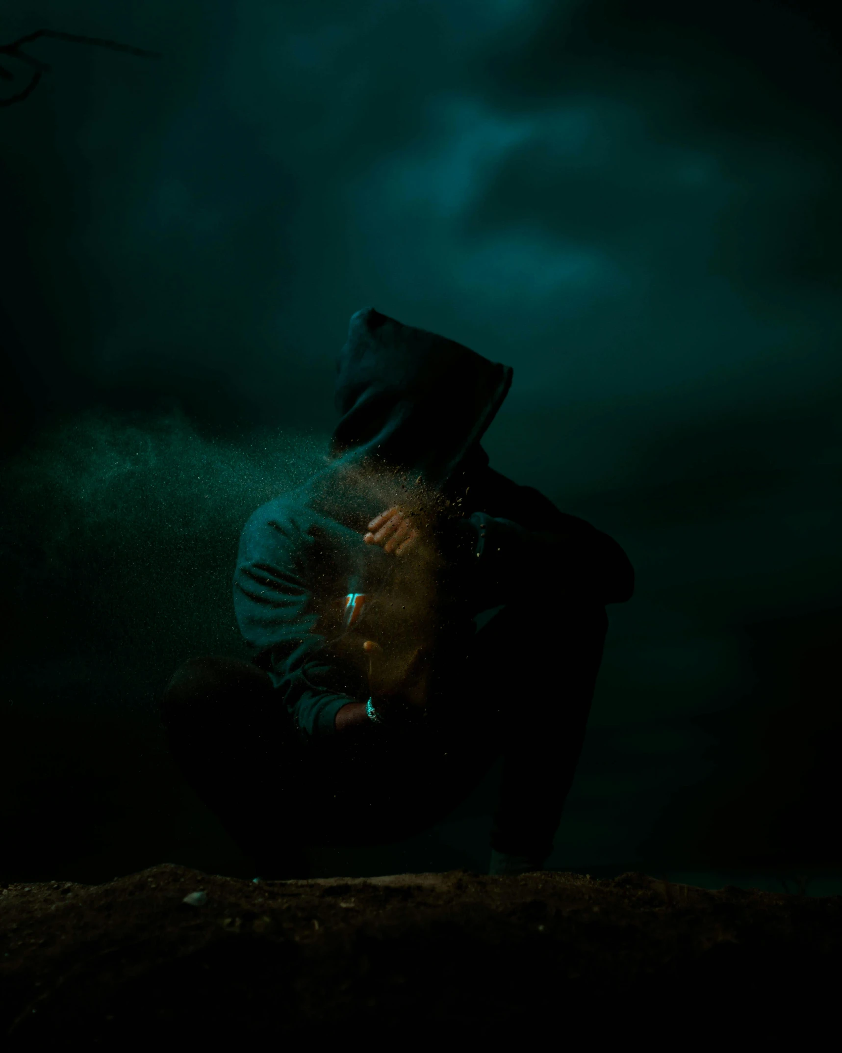 man in hoodie crouches against ground and dark sky