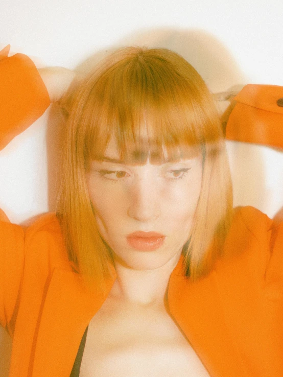 young woman with short red hair and large  poses with her hands to her forehead