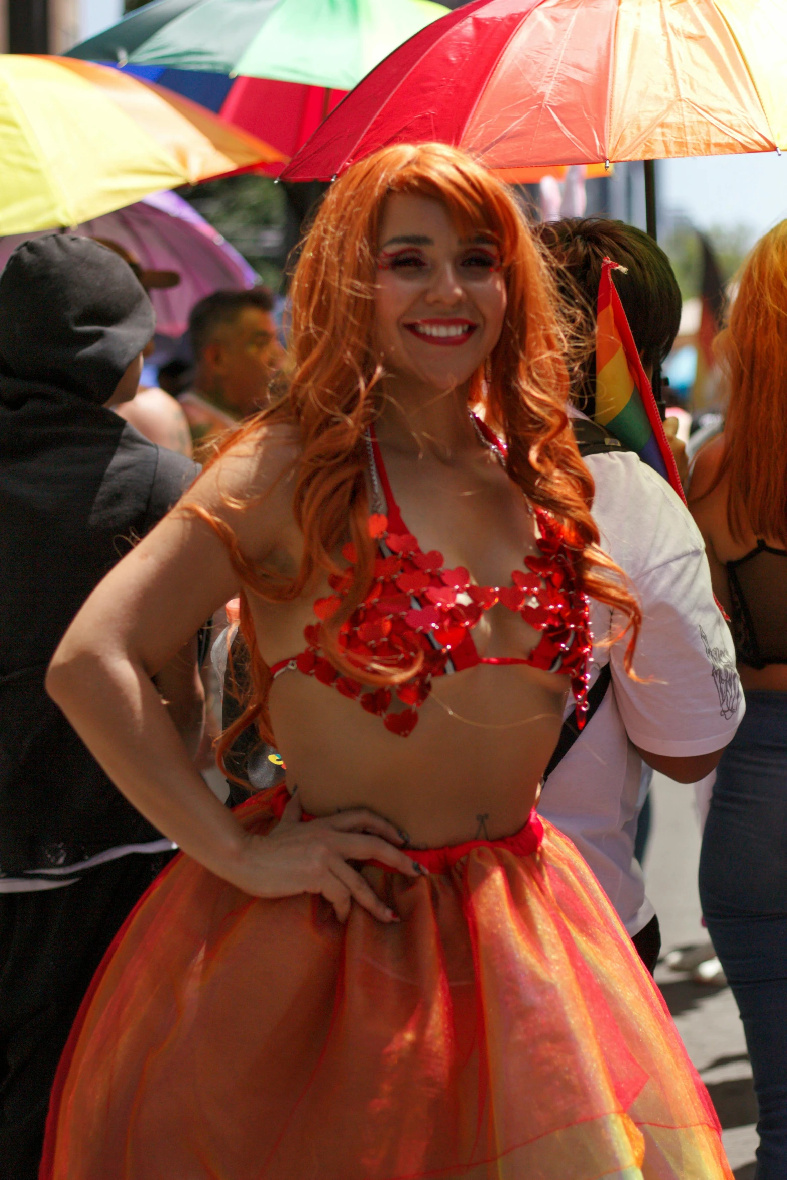 a woman in an orange dress poses on the street with her colorful umbrellas