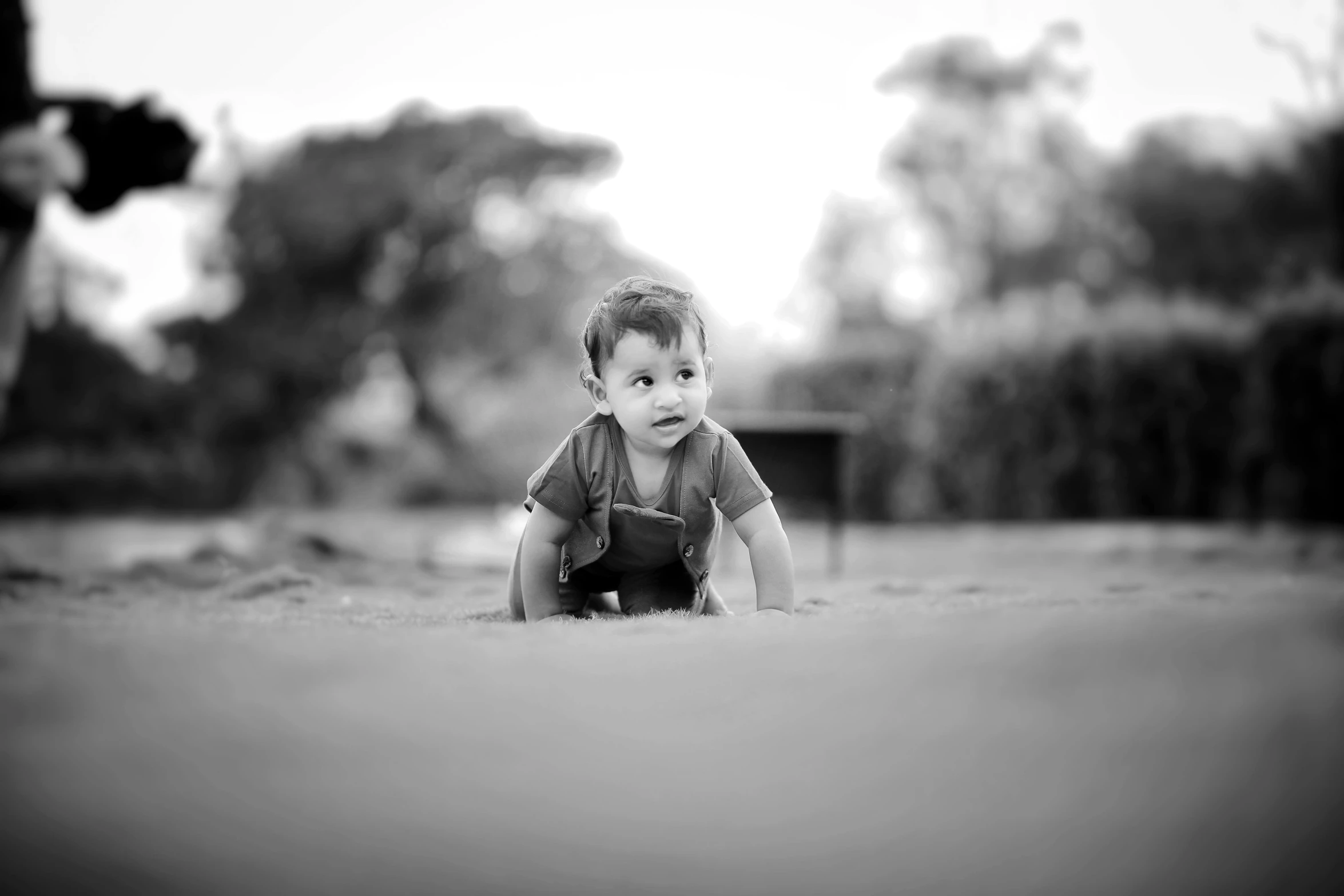 an infant wearing a dress crawling in a field