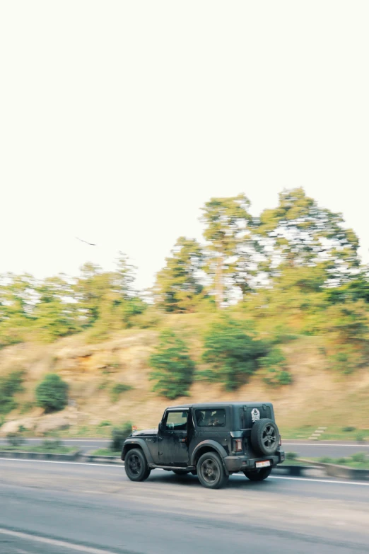 a jeep driving on a road past trees and bushes