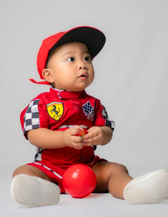 a baby with a red football outfit, a black hat and a ball