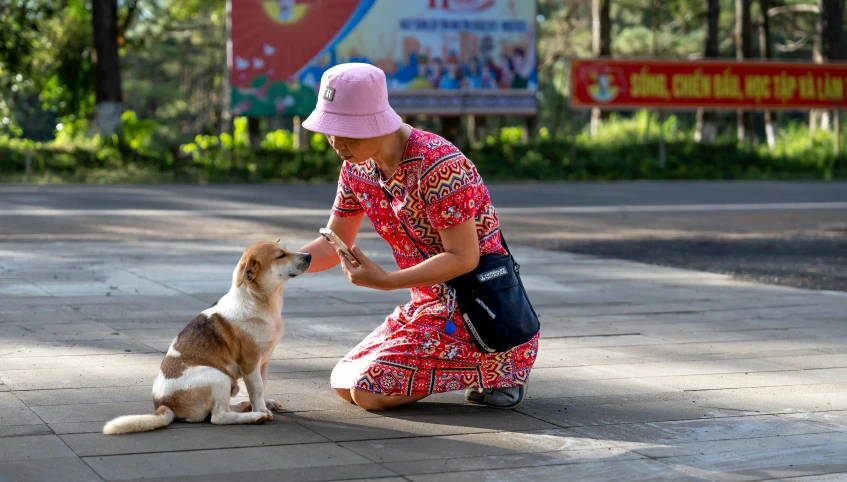 the woman kneels and pets the small dog