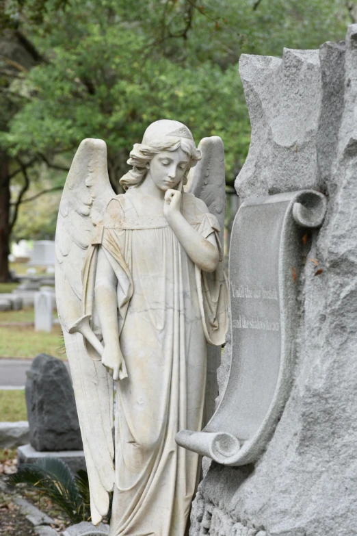 a white angel with hands in his pocket next to a stone fountain