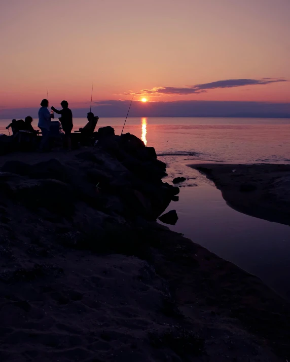 the group is fishing from the shore at sunset