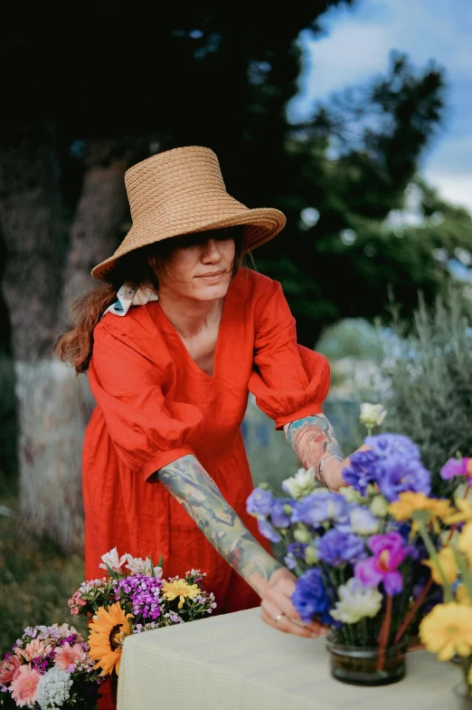 a woman in a hat reaches over a vase of flowers