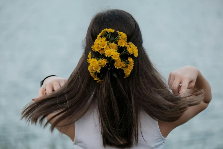 the back of a girl's head is seen with a yellow flower in her hair