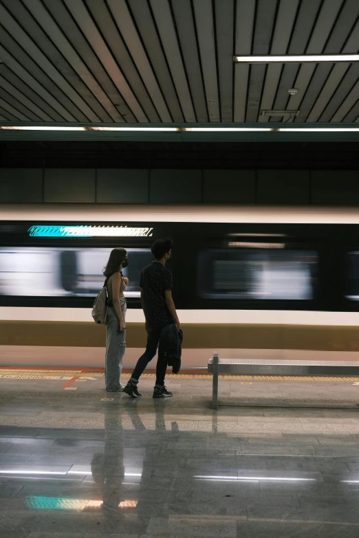 two people are walking past a subway as the train passes