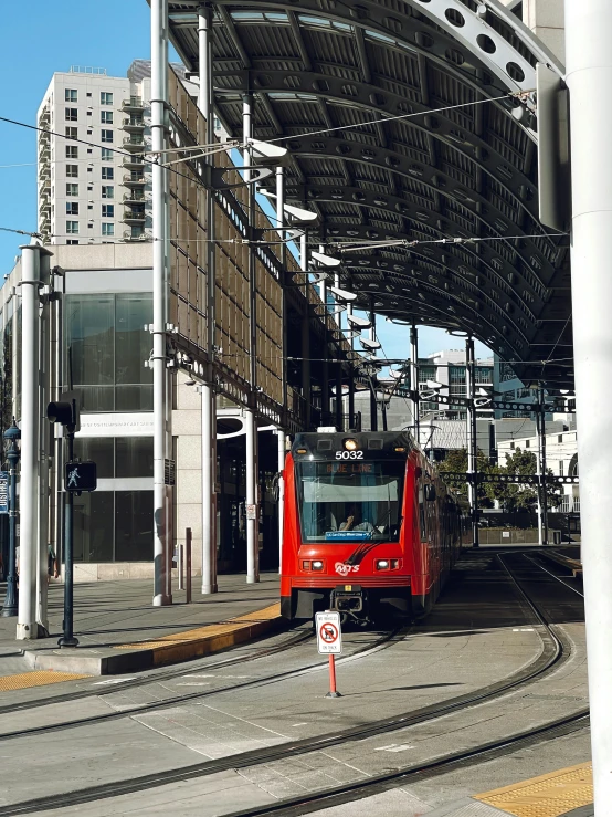 a red train traveling down train tracks next to a tall building