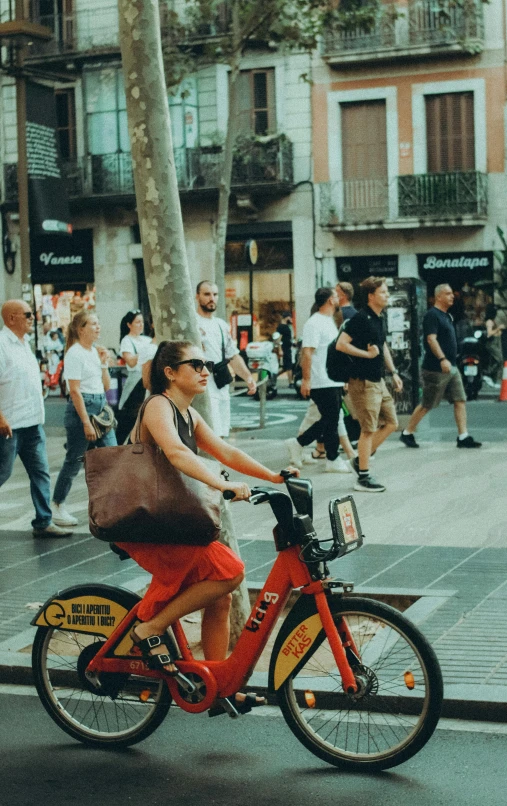 a woman riding on the back of a red bike down a street