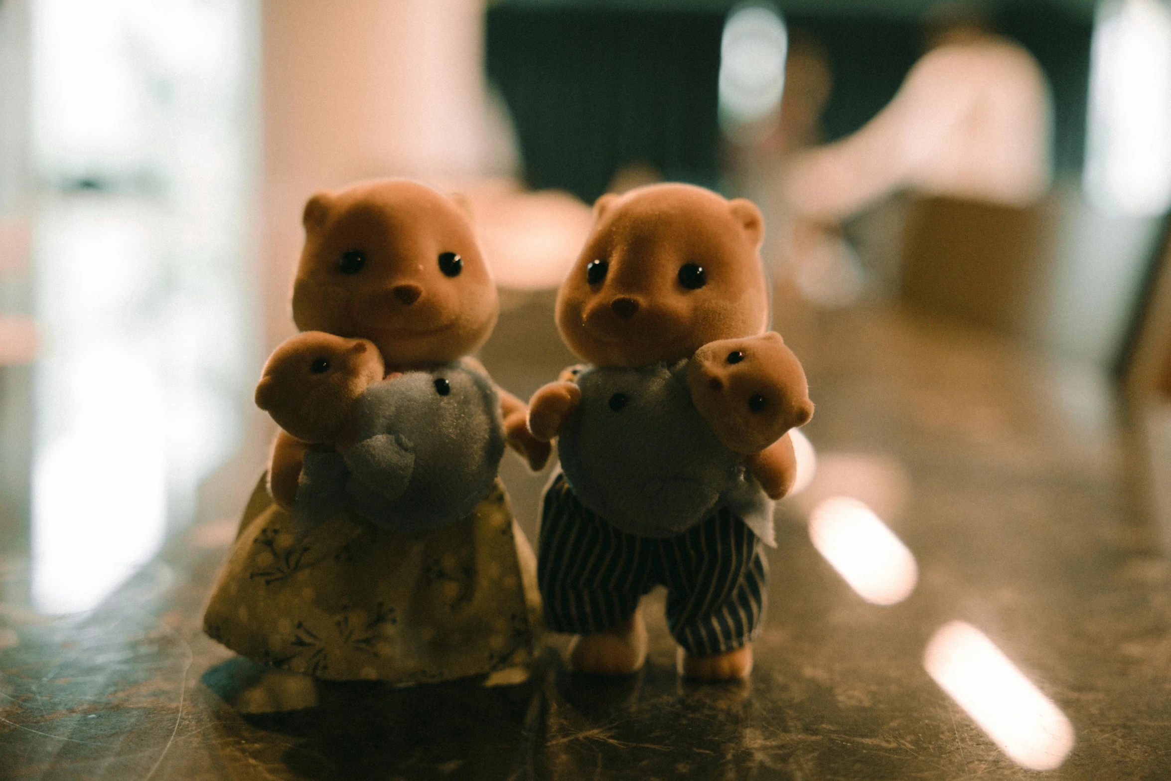 a small brown bear standing next to a smaller brown stuffed animal on top of a wooden table