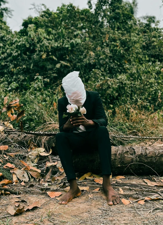 person in dark suit crouches, holding a flower