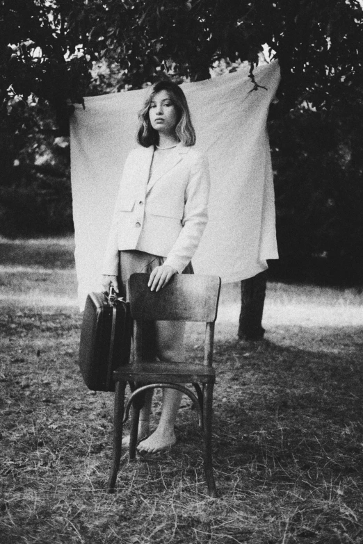 a woman poses in a chair while holding a suitcase