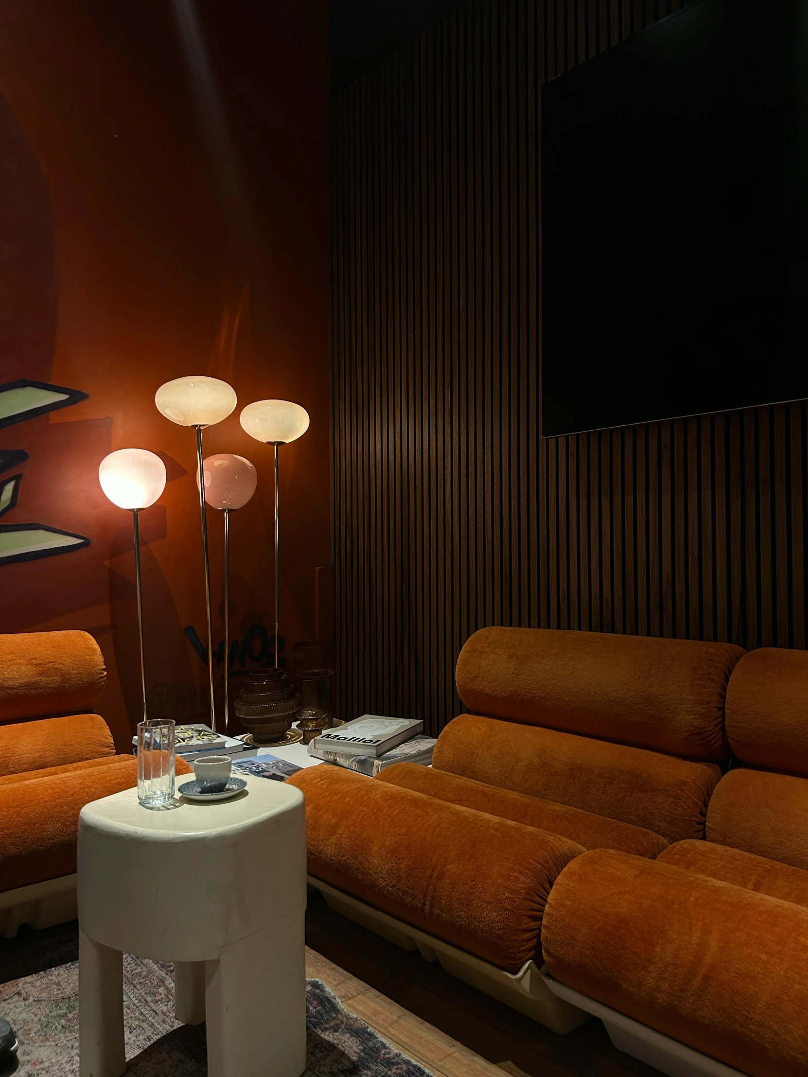 the room has three lights, one lamp on and two orange sofas