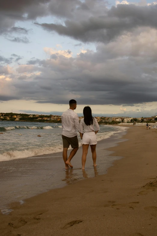 a man and woman walk along the beach holding hands