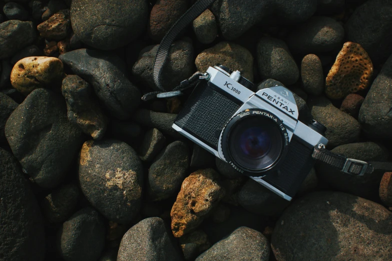 this camera is laying on some rocks near the ocean