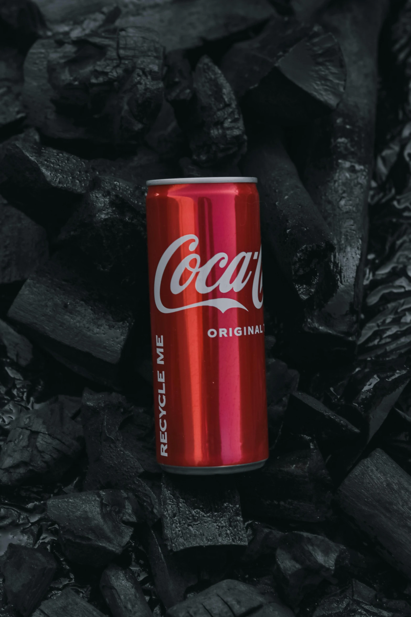 coke can lying on black coal with the lid removed