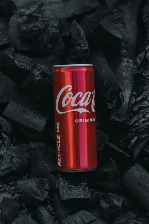 coke can lying on black coal with the lid removed