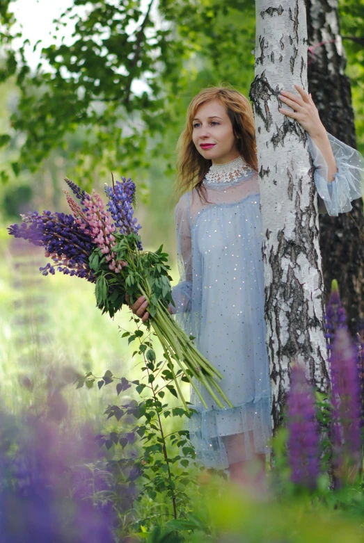 a woman is standing beside a tree, with purple flowers