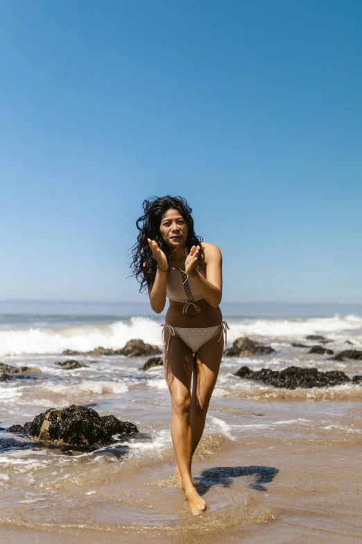 a woman wearing a tan bikini walking on the beach