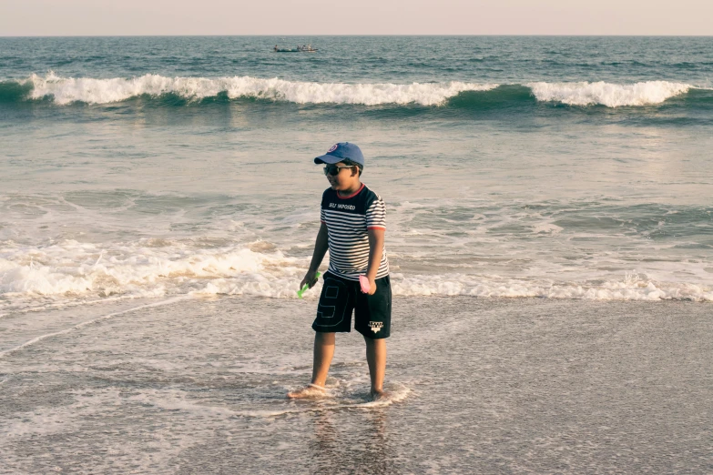 a boy is standing on the beach looking at the waves
