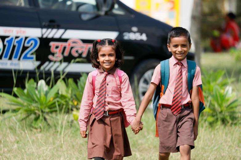 two young children walking in the grass with backpacks on