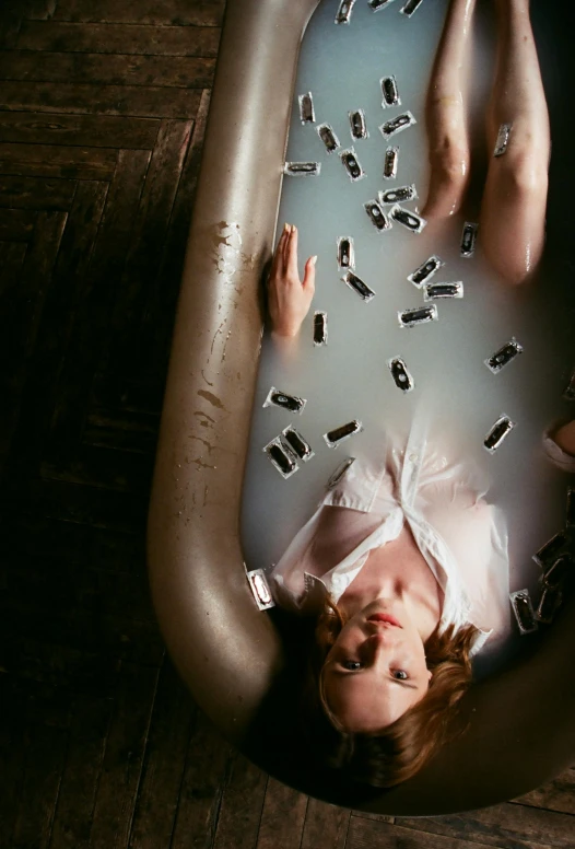 the woman lays in a bathtub surrounded by random objects