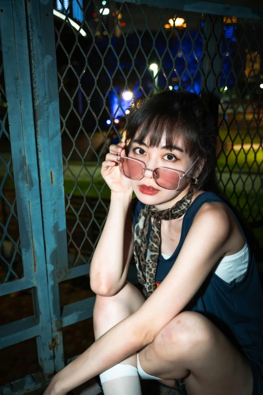 a woman sitting next to a fence holding her hands up