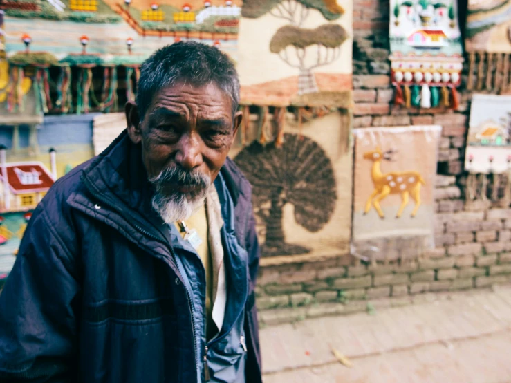 an old man wearing a blue jacket standing on the sidewalk