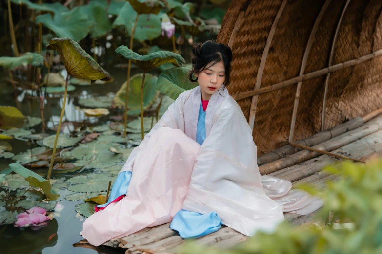 an asian woman is in a white and blue outfit sitting on a bamboo raft