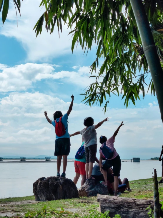 four people standing on a cliff with their arms raised