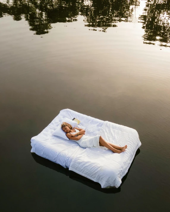 a woman in white lies down on a floating bed