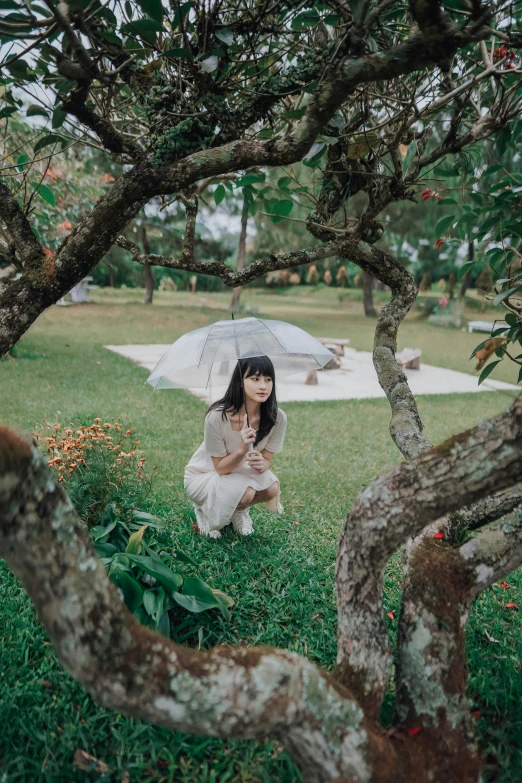 a woman in a white dress kneeling under an umbrella on grass