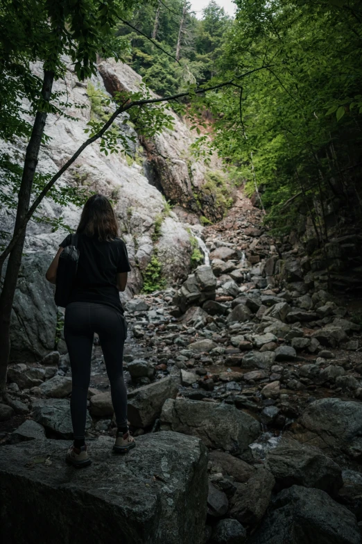 a woman with a backpack stands on rocks near a waterfall