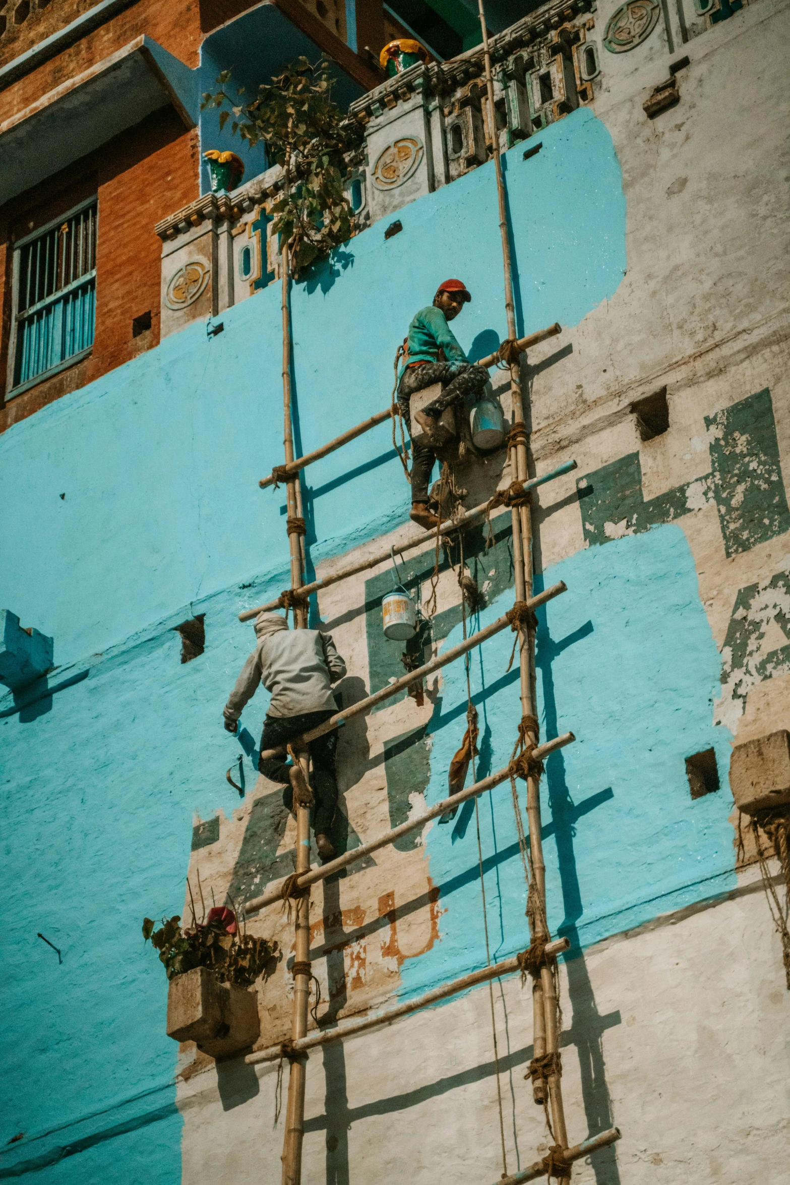 two people are painting the side of a blue building