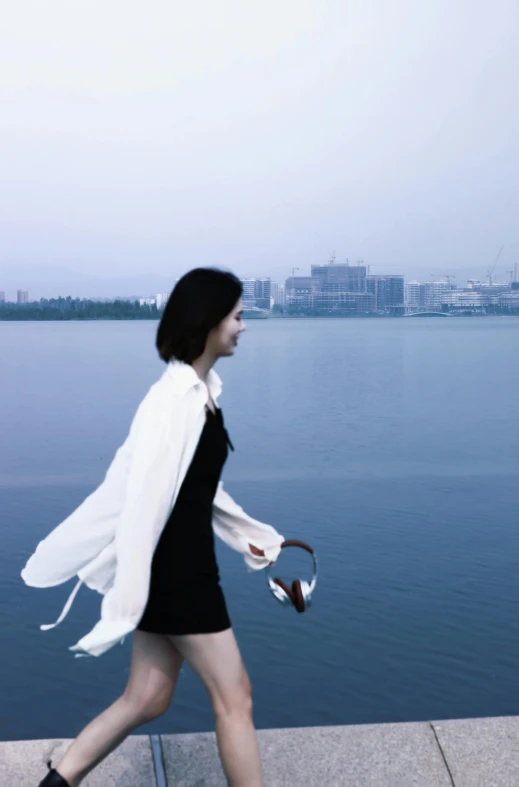 a woman is walking near the water, by the shore