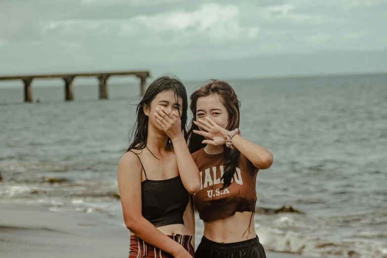 two girls making faces as they stand on the beach