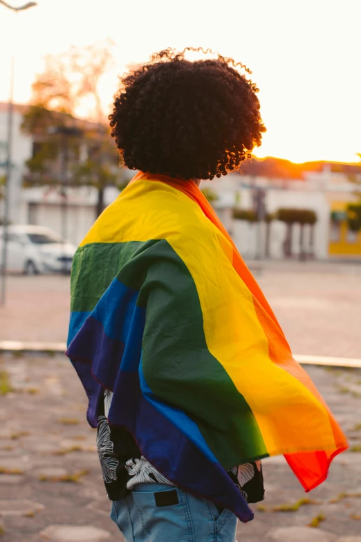 a person standing in the street, with a rainbow flag wrapped around their shoulders