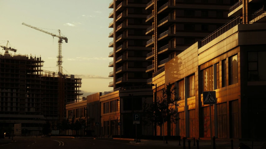 construction cranes are silhouetted against the evening sky on a city street