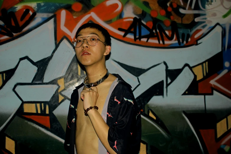 young man wearing glasses holding a necklace and looking away