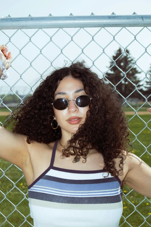 a woman posing in front of a fence wearing black sunglasses