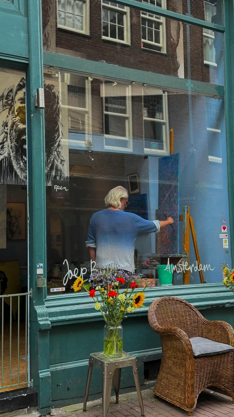 an old woman standing at a window with some flower arrangement