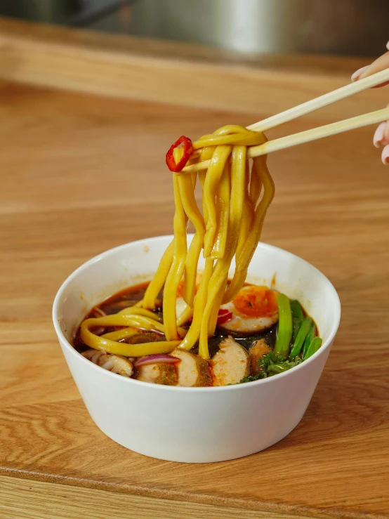 a person holding chopsticks over noodles with vegetables in a bowl