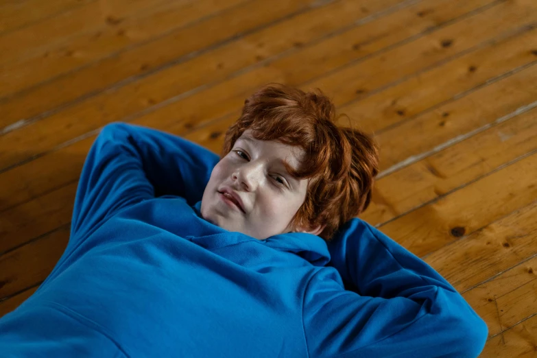 a  in blue sweatshirt laying on a wooden floor