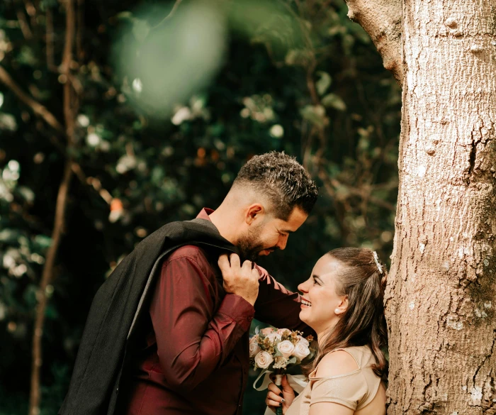 a couple standing next to each other next to a tree