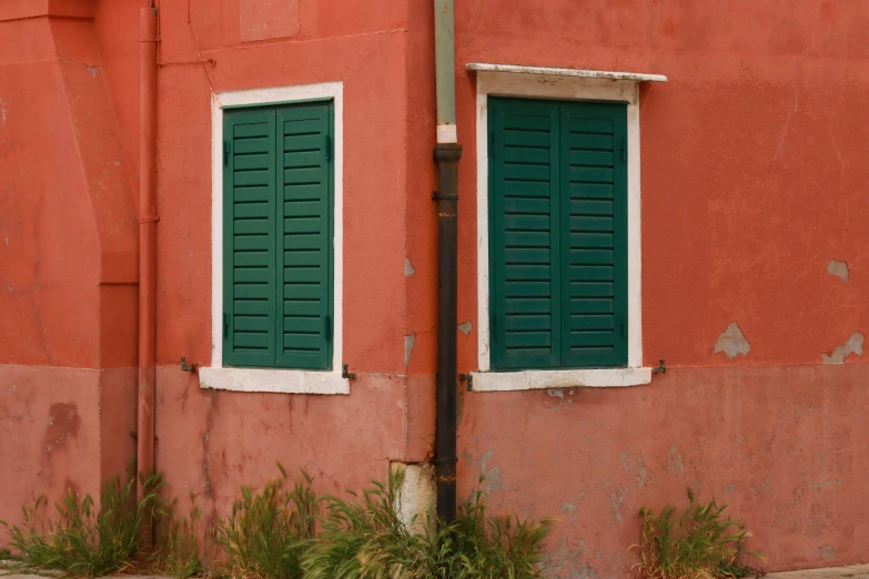 a red building with two large windows and two green shutters